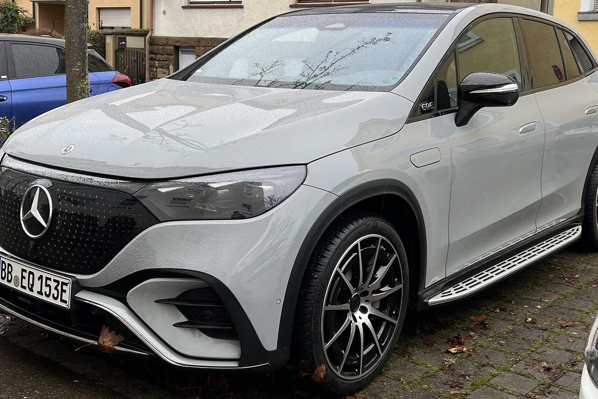 A light grey Mercedes-Benz EQE SUV with black multi-spoke wheels, parked on a cobblestone street with fallen leaves