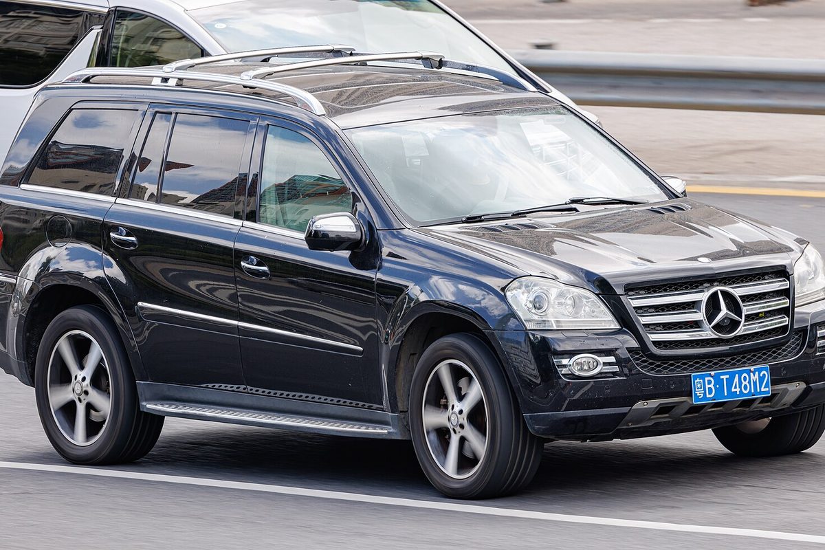 A black first-generation Mercedes-Benz GL-Class SUV with roof rails, driving on a city road