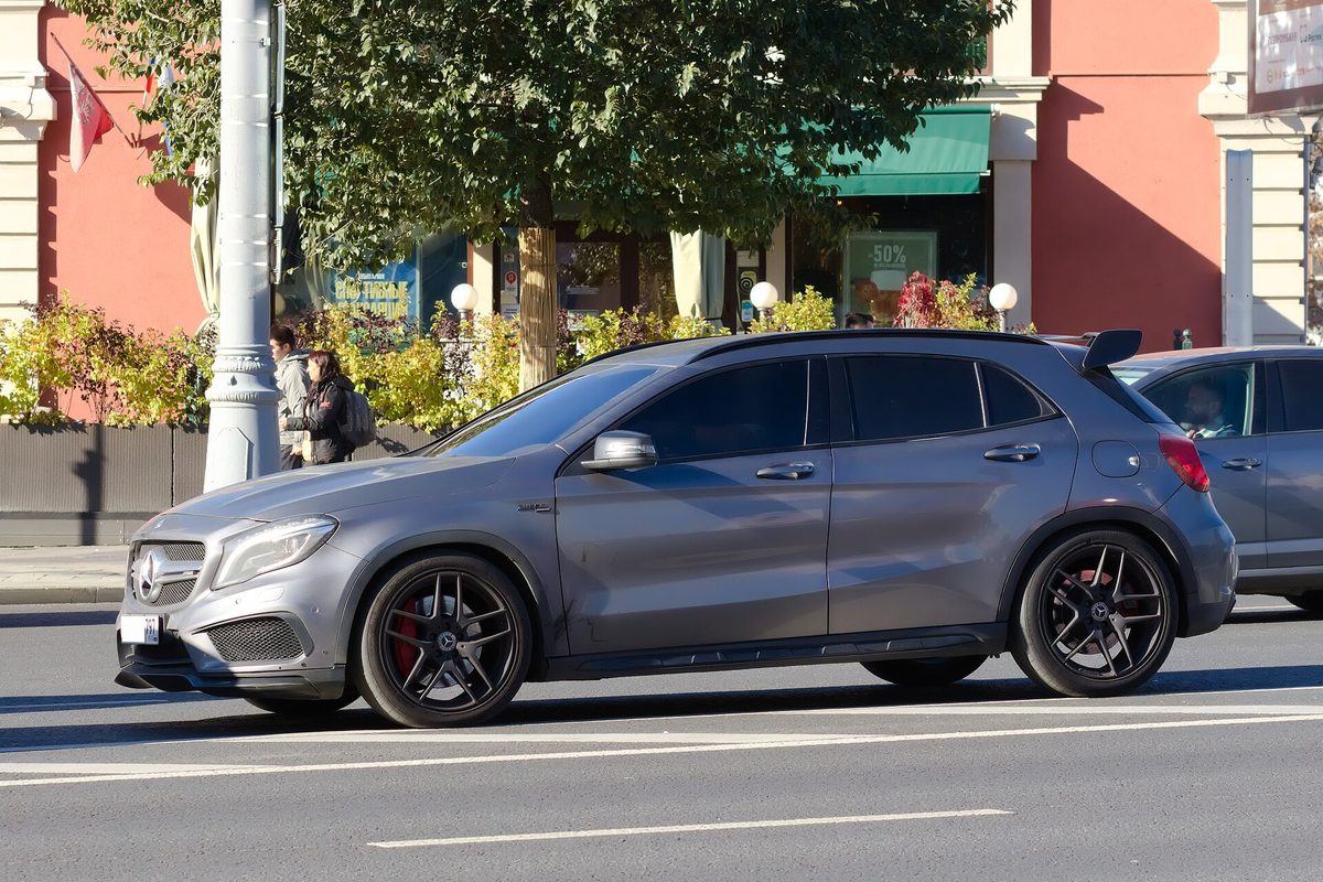 A grey Mercedes-Benz GLA crossover with black wheels and red brake calipers driving down a city street