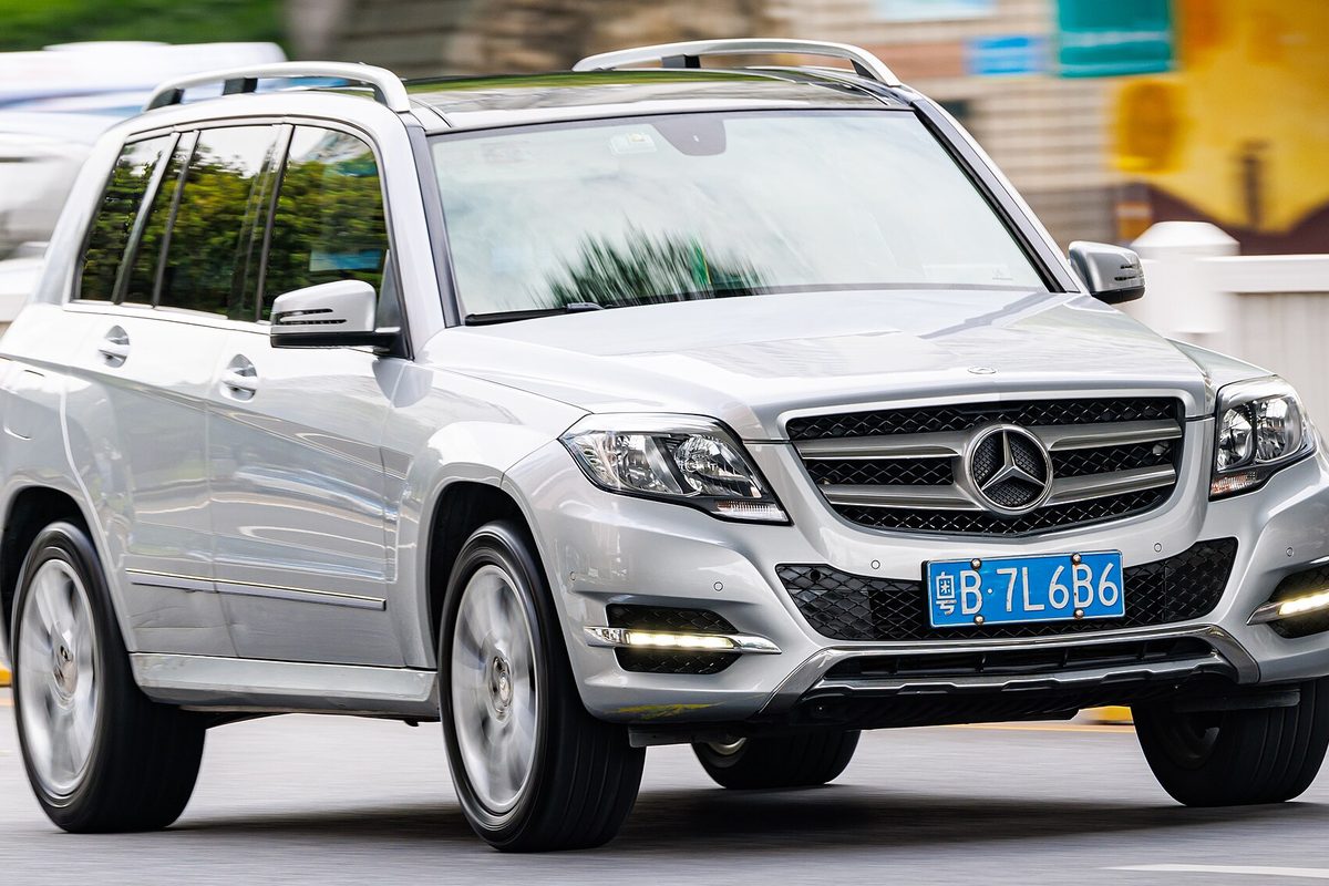 A silver X204 Mercedes-Benz GLK-Class SUV with roof rails and LED running lights, driving on a city street