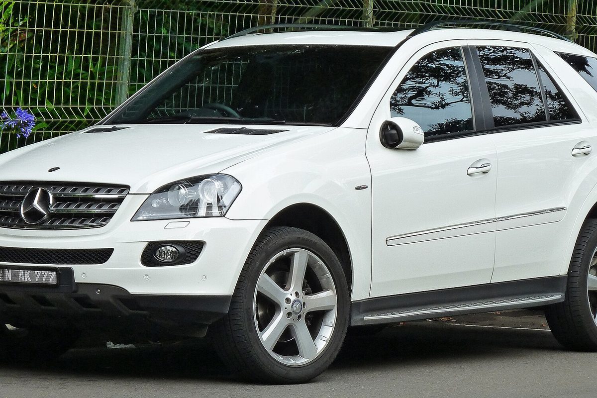 A white 2008 Mercedes-Benz ML 320 CDI SUV with five-spoke alloy wheels, parked beside a green wire fence