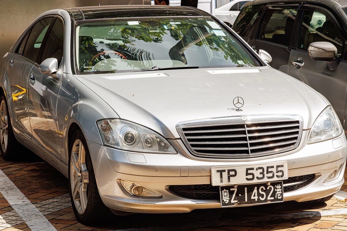 A silver W221 Mercedes-Benz S-Class sedan parked on a brick-paved lot beside other cars