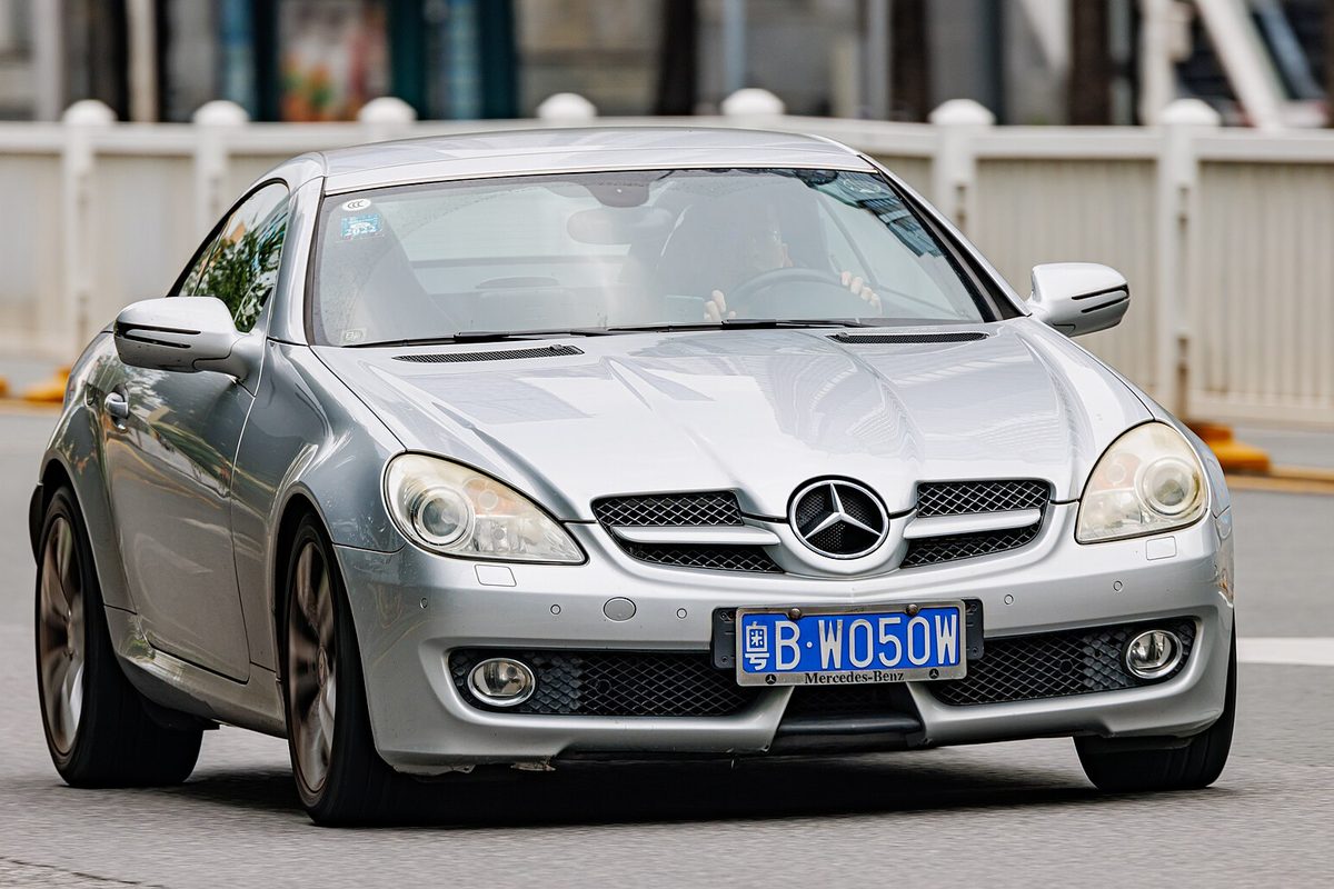 A silver Mercedes-Benz SLK roadster with its hardtop closed, driving on a city street