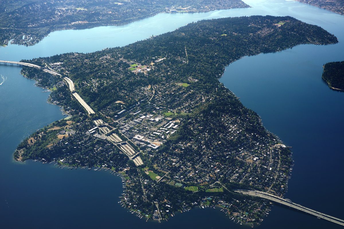 Aerial view of Mercer Island from the northwest, its wooded neighborhoods ringed by Lake Washington and crossed by the Interstate 90 bridges