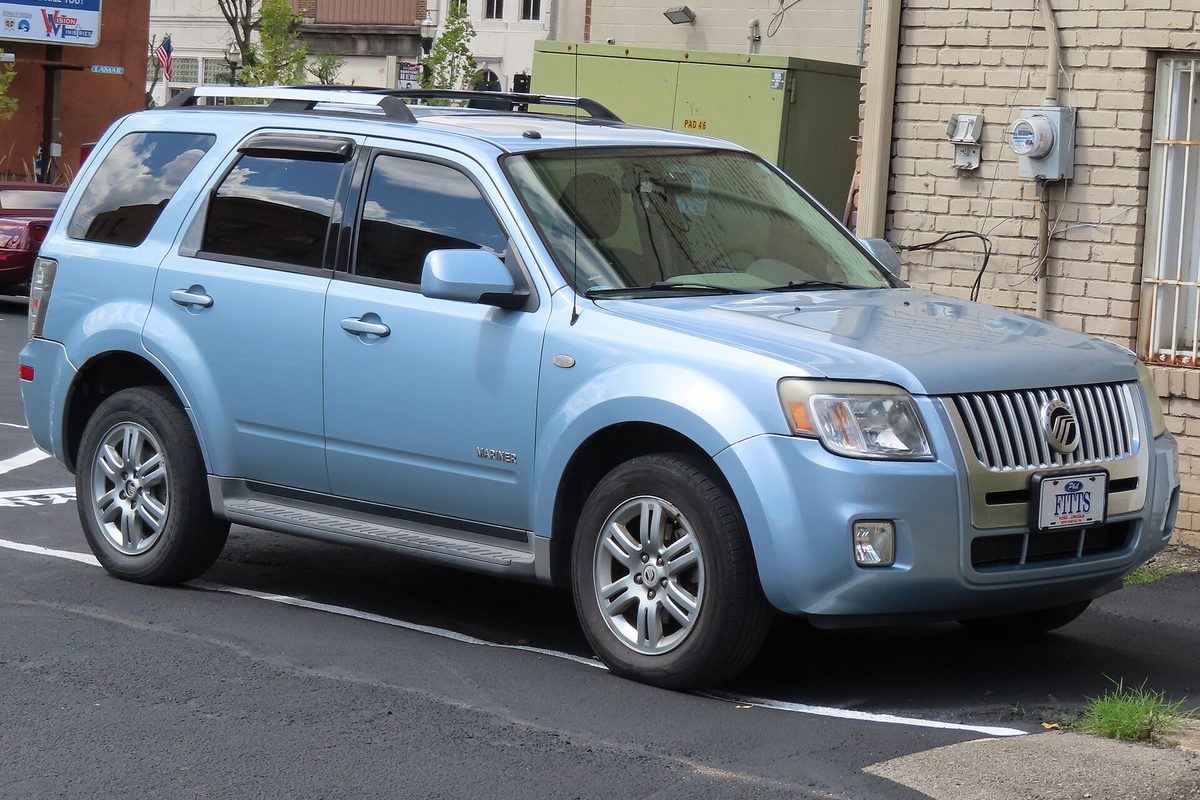 A light blue 2008 Mercury Mariner Premier SUV with a chrome grille and roof rails, parked in a lot beside a brick building