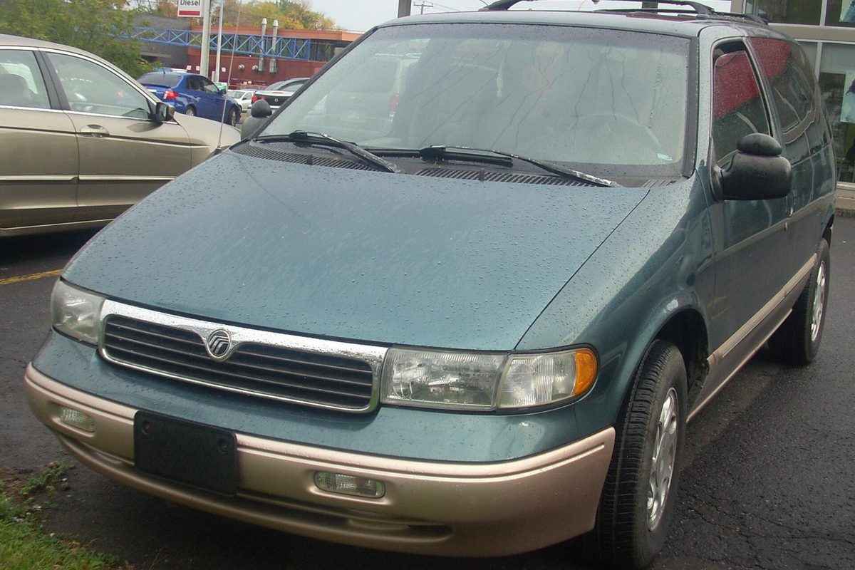 A teal 1996-1998 Mercury Villager minivan with tan lower bumpers and trim, wet with rain in a parking lot