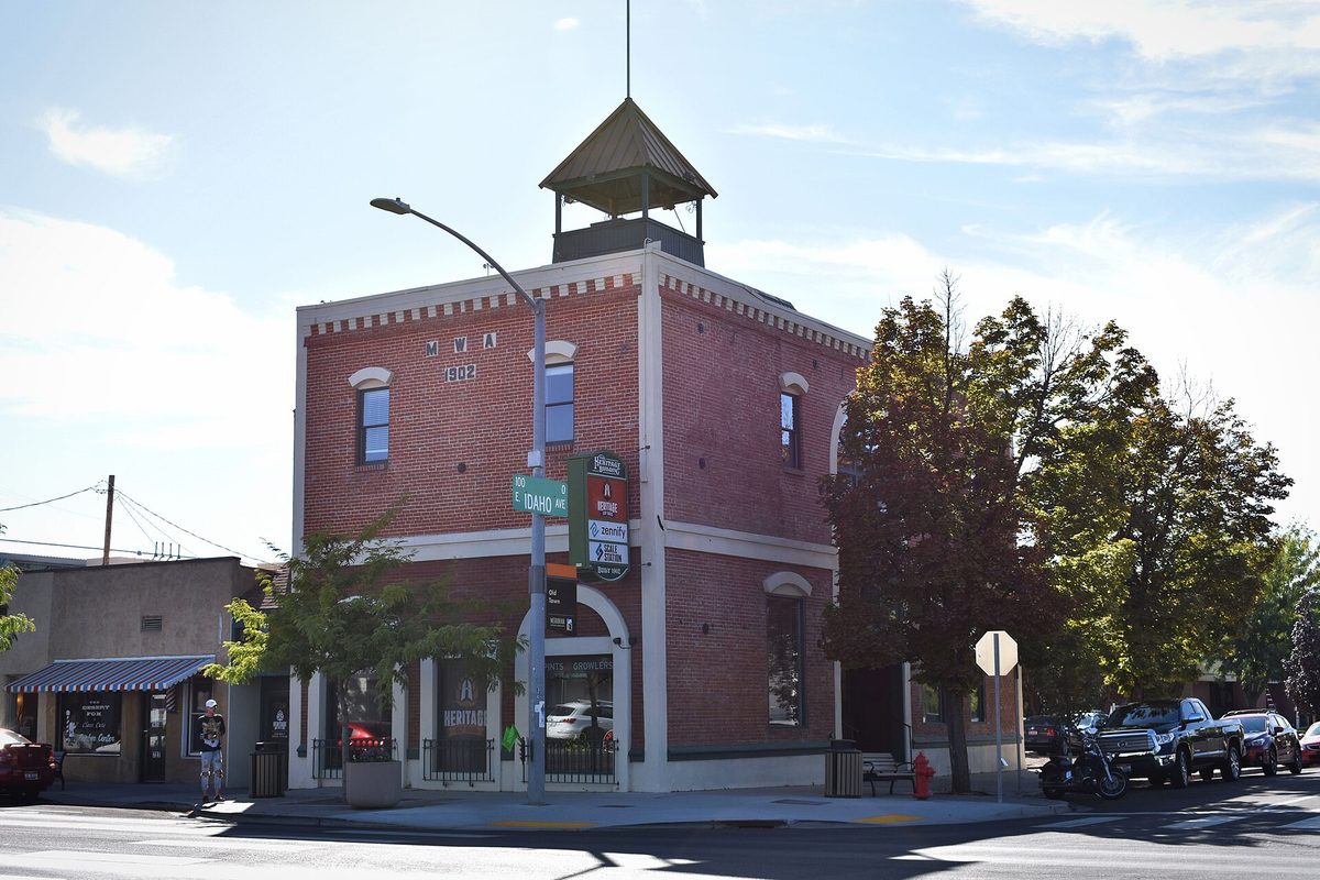 The two-story red brick Heritage Building on a corner in downtown Meridian, with a small cupola on its roof and street signs out front