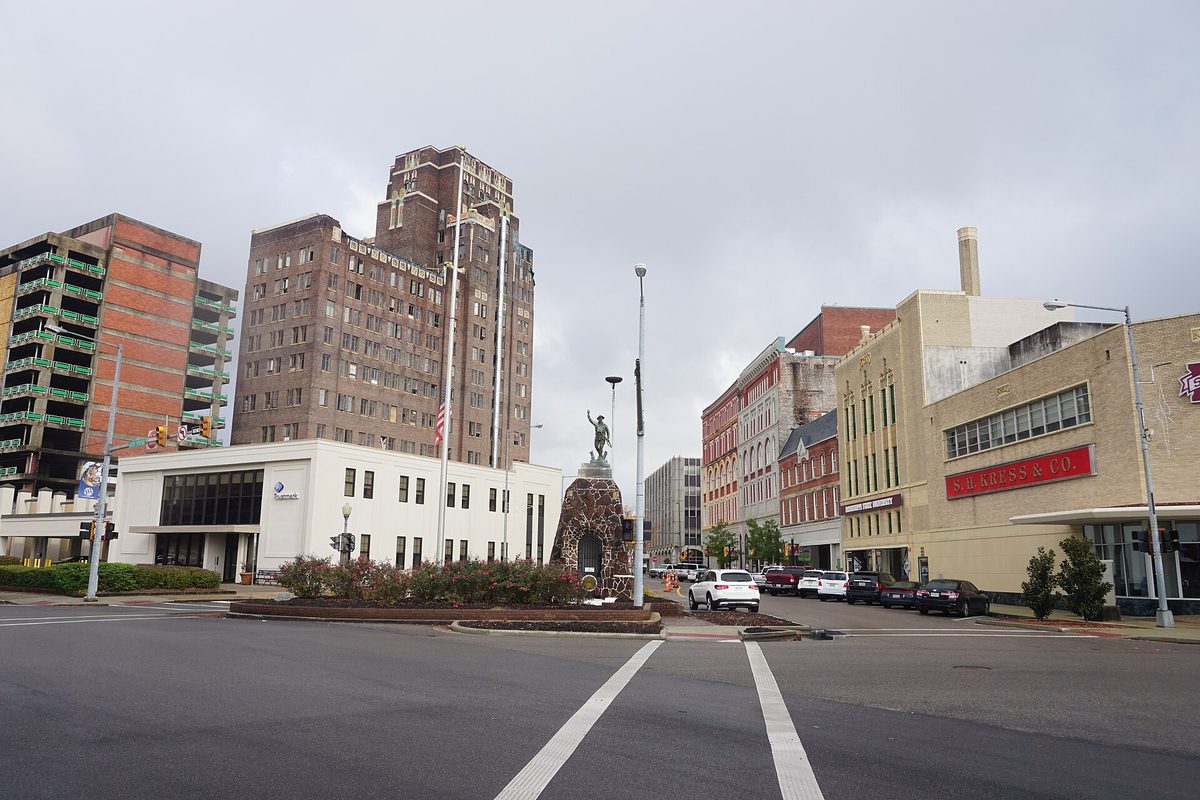 Downtown Meridian on 6th Street under a gray sky, with older high-rise buildings and a statue on a planted median
