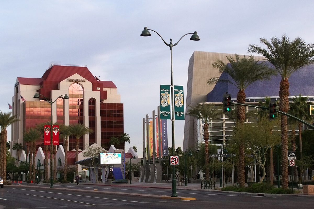 The red-roofed Mesa Bank building and the Mesa Arts Center behind palm trees and street-lamp banners in downtown Mesa