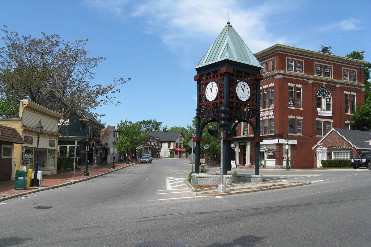 The ornate clock tower with a green copper roof in Gaunt Square, Methuen, beside a red brick building and a quiet street