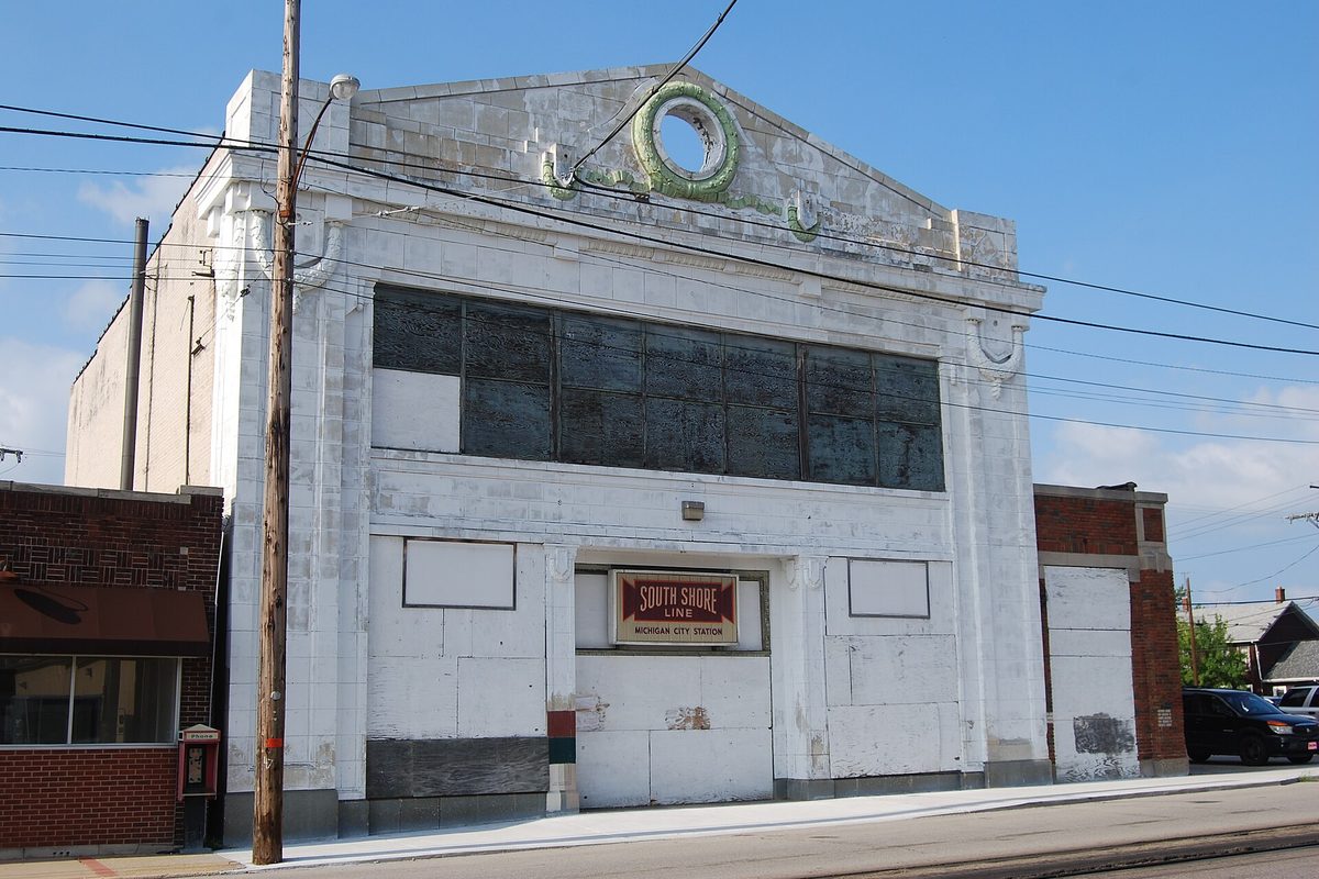 The white former South Shore Line station in Michigan City, its windows boarded over, with a South Shore Line sign above the door
