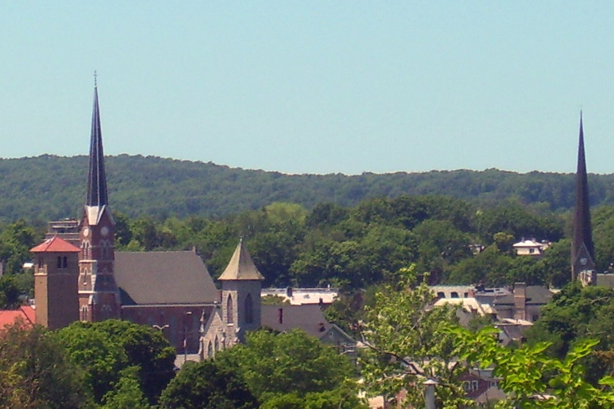 Downtown Middletown with the tall dark spire of the First Congregational Church and a brick church tower in front of green wooded hills