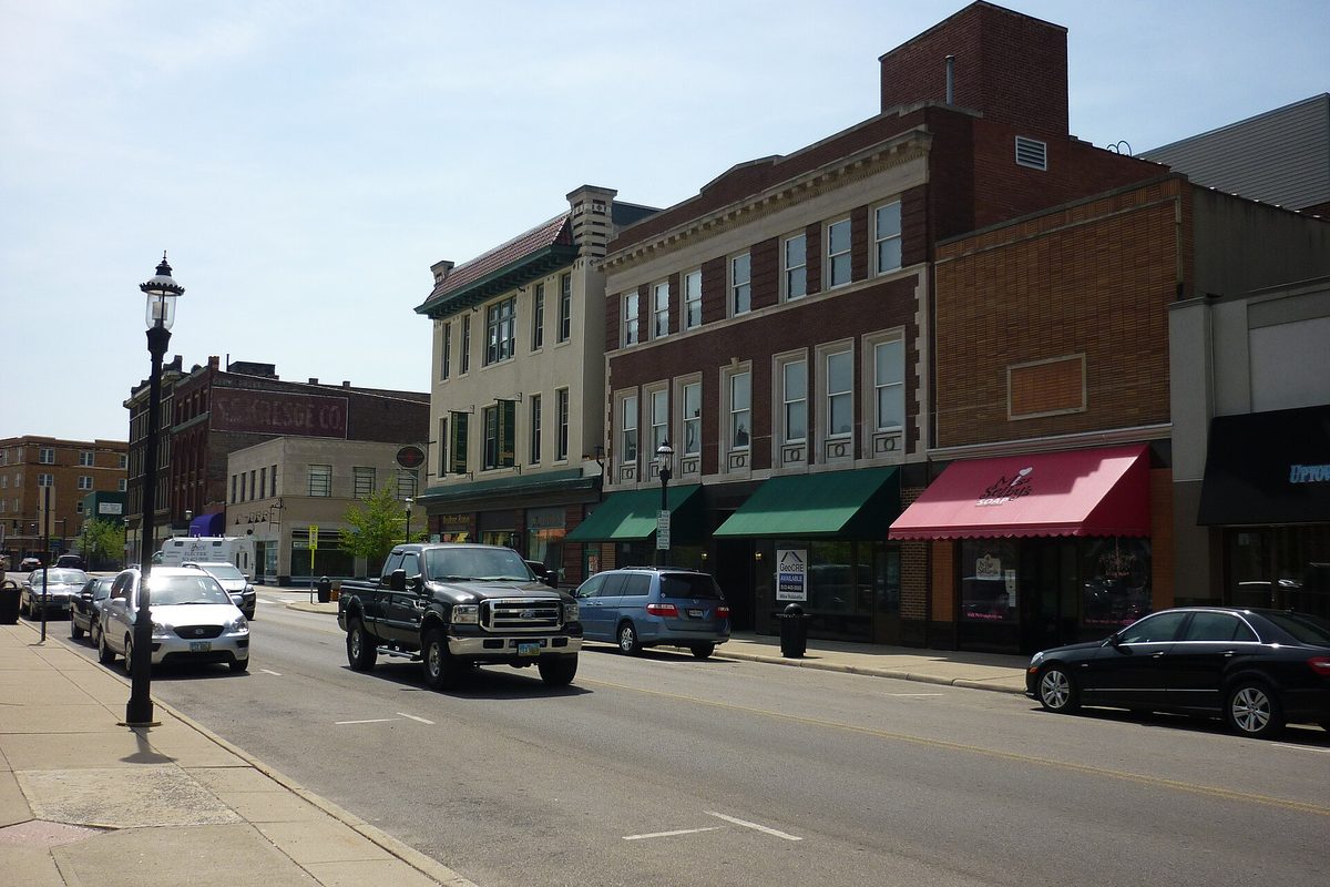 A sunny block of downtown Middletown with two- and three-story brick storefronts under green and red awnings, a pickup truck and cars parked at the curb