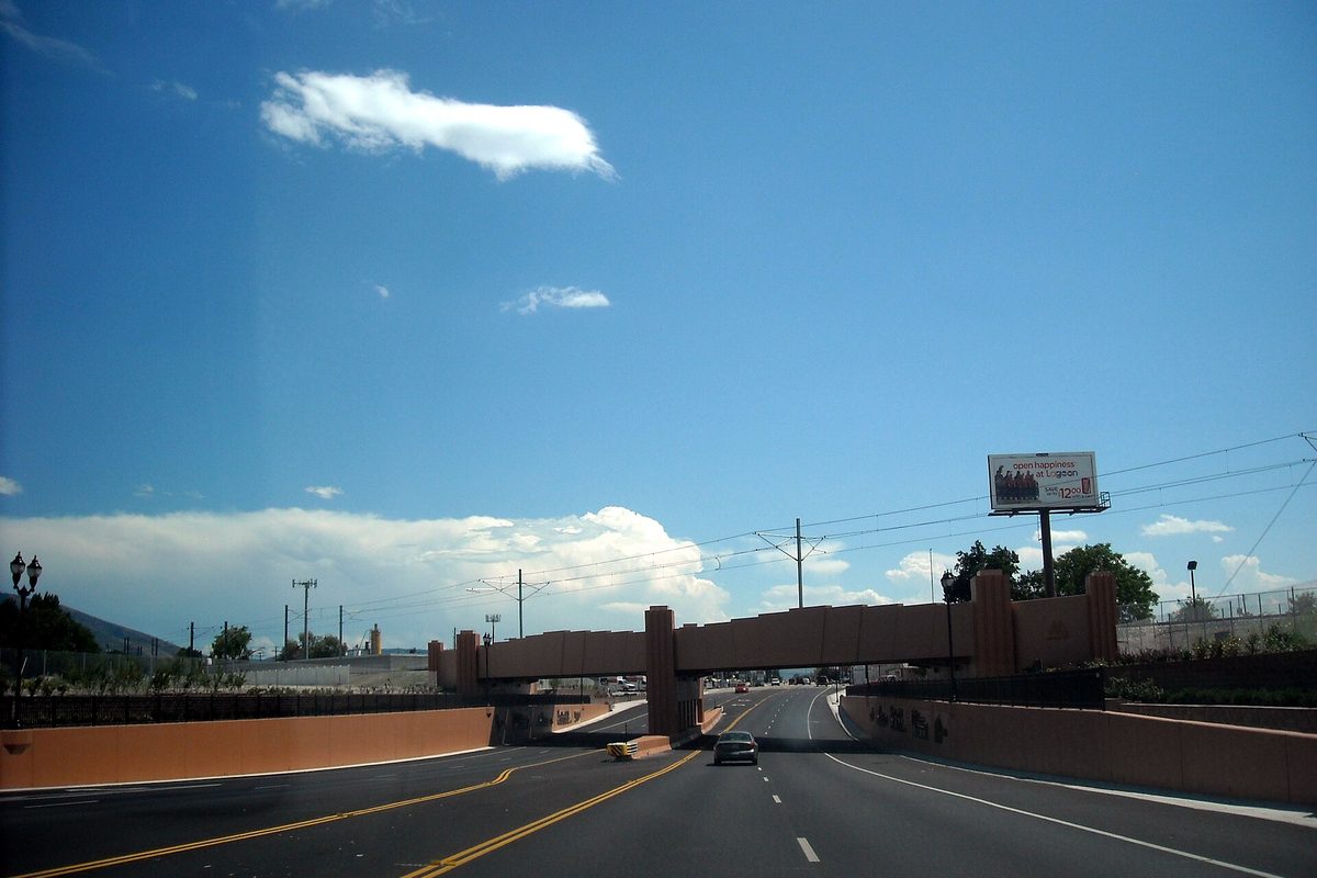 State Street southbound in Midvale, a divided road passing under a tan concrete overpass beneath a blue sky with white clouds