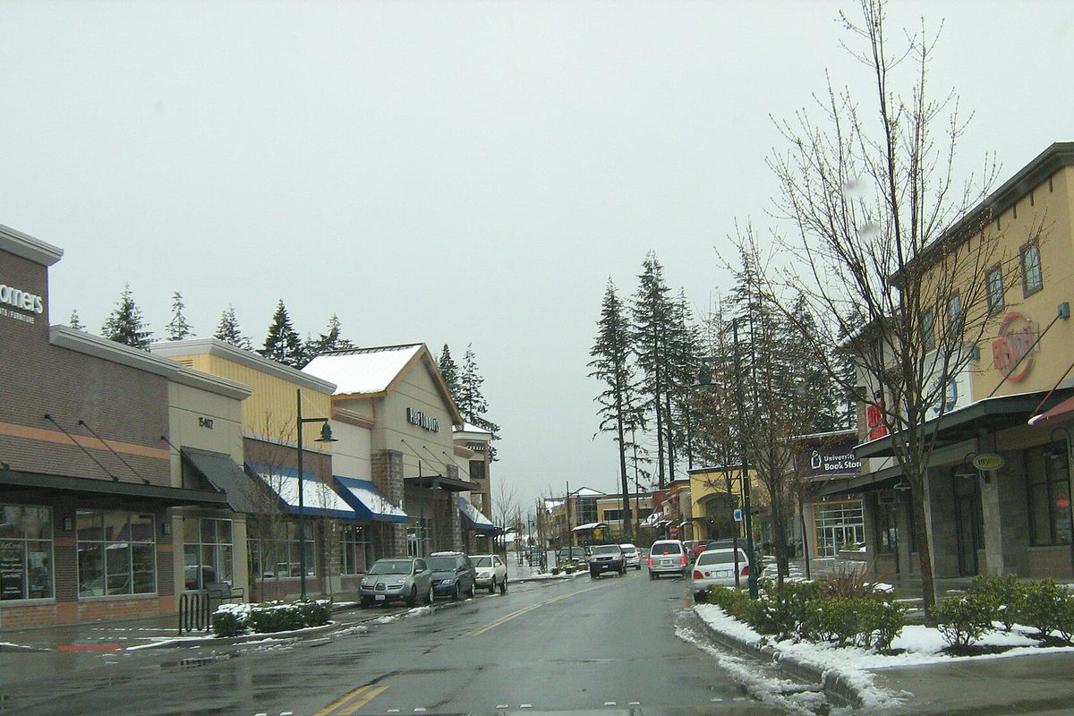 Main Street through Mill Creek Town Center with awnings over the shops, a light snow on the roofs and curbs, and tall evergreens behind