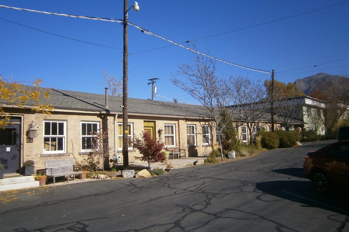 Part of the former Baldwin Radio Factory in Millcreek, a long low tan brick building with white-trimmed windows, bare trees and a mountain peak behind