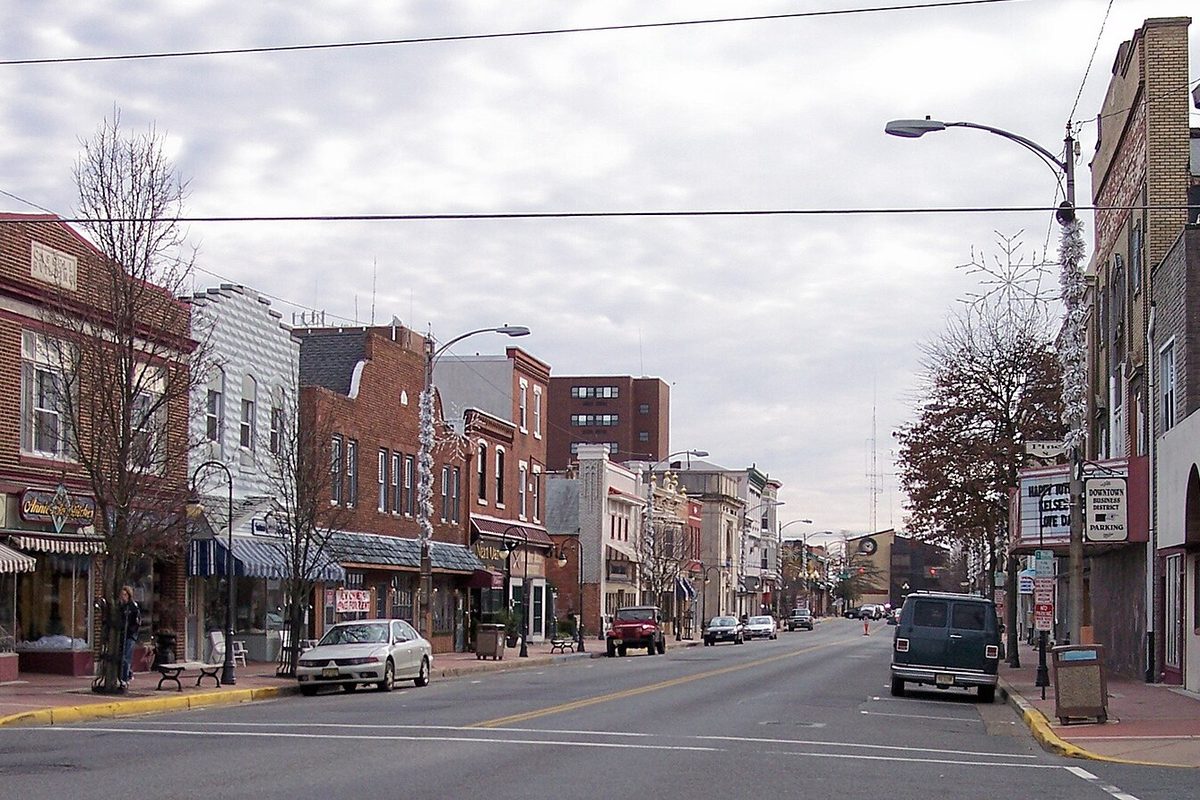 High Street in downtown Millville, lined with two- and three-story brick storefronts with awnings, bare trees and a few parked cars under a gray sky
