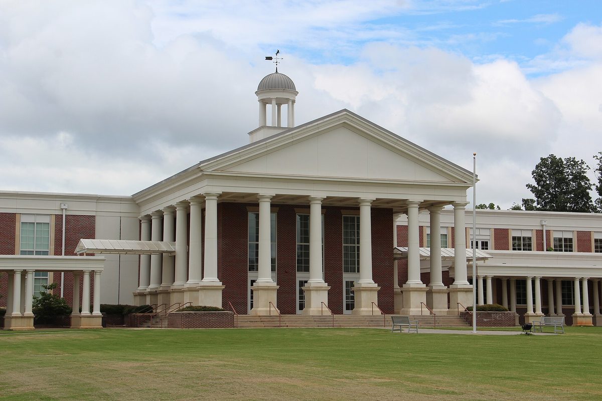 Milton High School's white portico with tall columns and a cupola topped by a weather vane, behind a wide green lawn