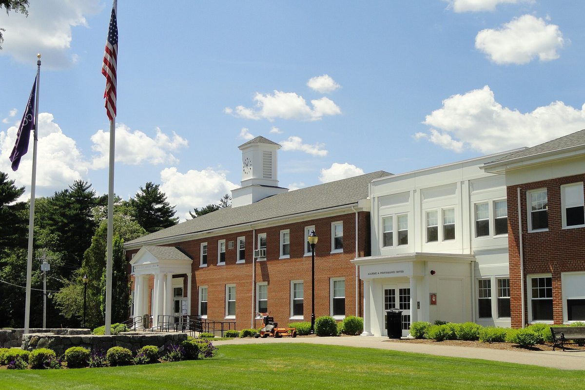 Curry College's Academic and Performance Center in Milton, a brick building with a white clock cupola, flags and a green lawn
