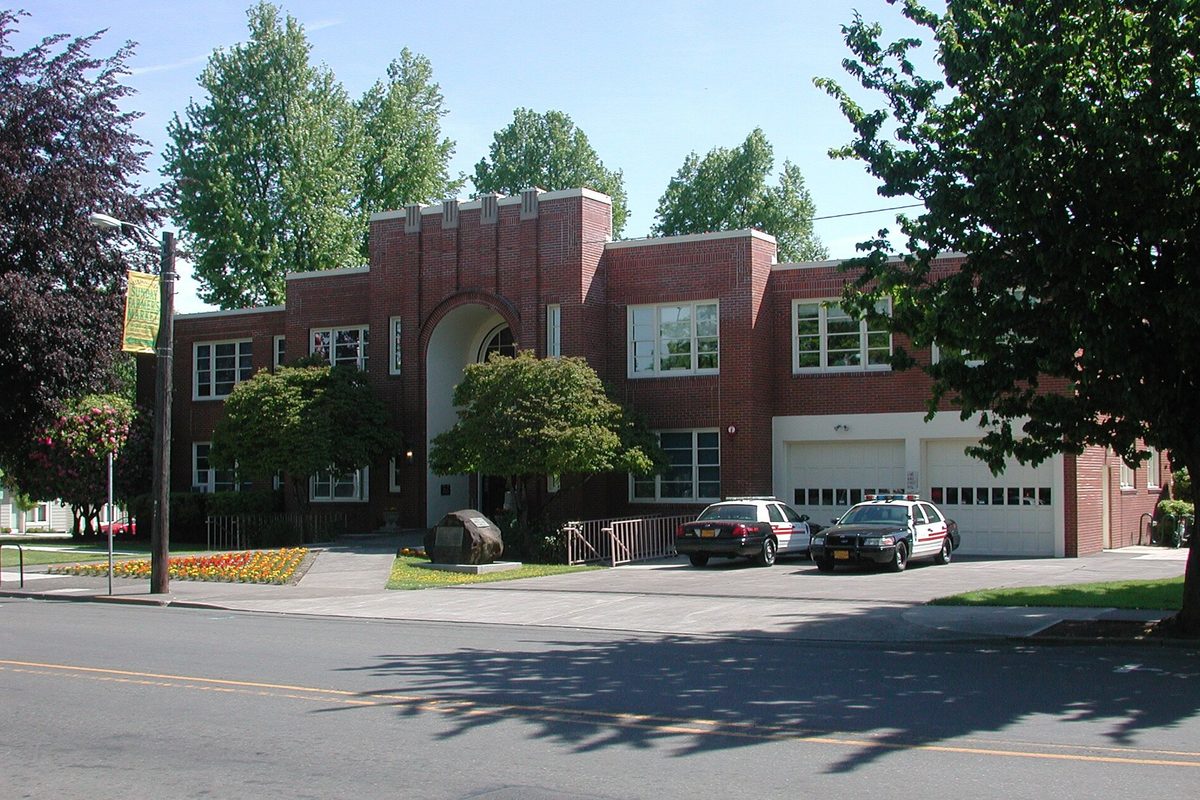 Milwaukie City Hall, a red brick building with an arched entry, seen from Main Street with two police cars parked beside it