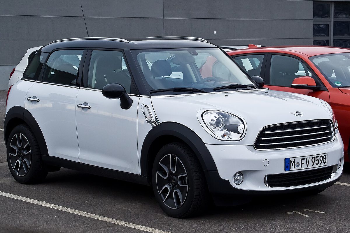 A white first-generation MINI Countryman with a black roof and black wheel-arch trim, parked in a lot beside a red car