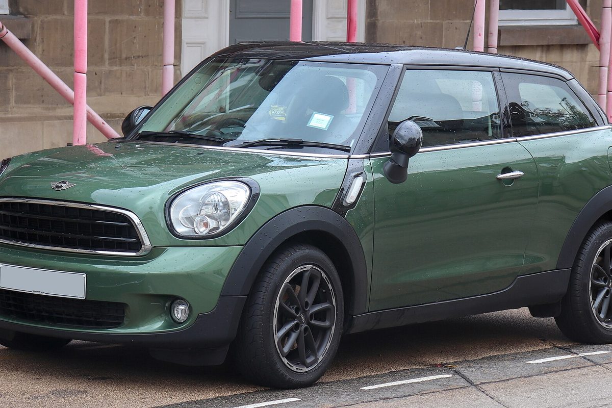 A dark green MINI Paceman with black wheel arches and dark alloy wheels, parked in front of a building with pink scaffolding poles