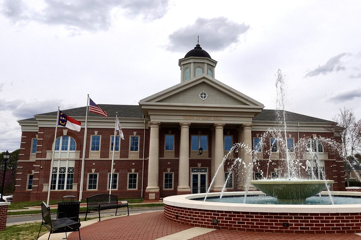 Mint Hill's brick town hall with white columns and a domed cupola, flags out front and a round fountain spraying water in the foreground