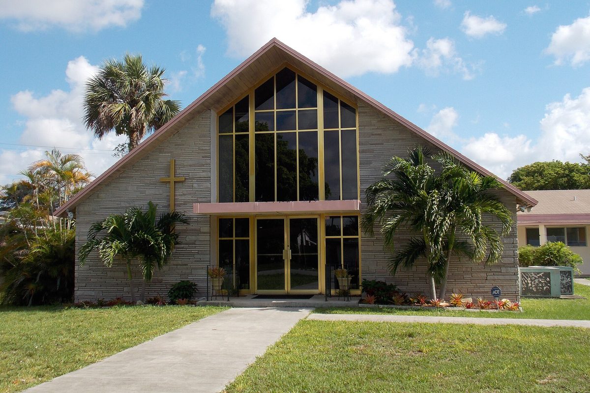 The Cathedral Church of the Resurrection in Miramar, a steep-gabled stone church with tall gold-framed windows, a gold cross and palm trees