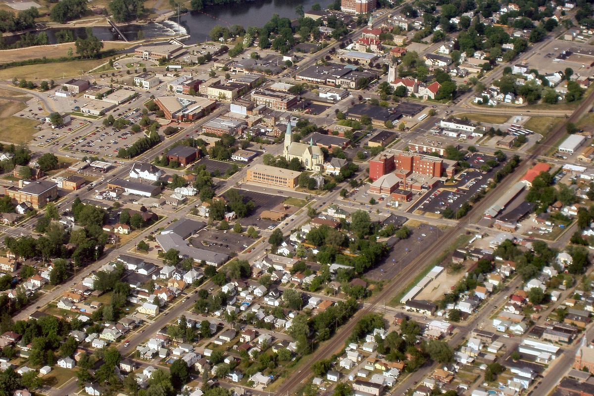 Aerial view of downtown Mishawaka south of the St. Joseph River, with a church steeple, a red brick building, parking lots and blocks of houses