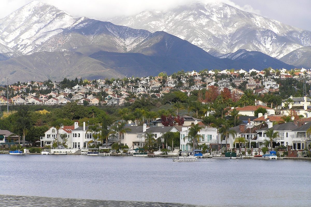 Snow-covered Saddleback peaks rising behind hillside homes and the waterfront houses along Lake Mission Viejo