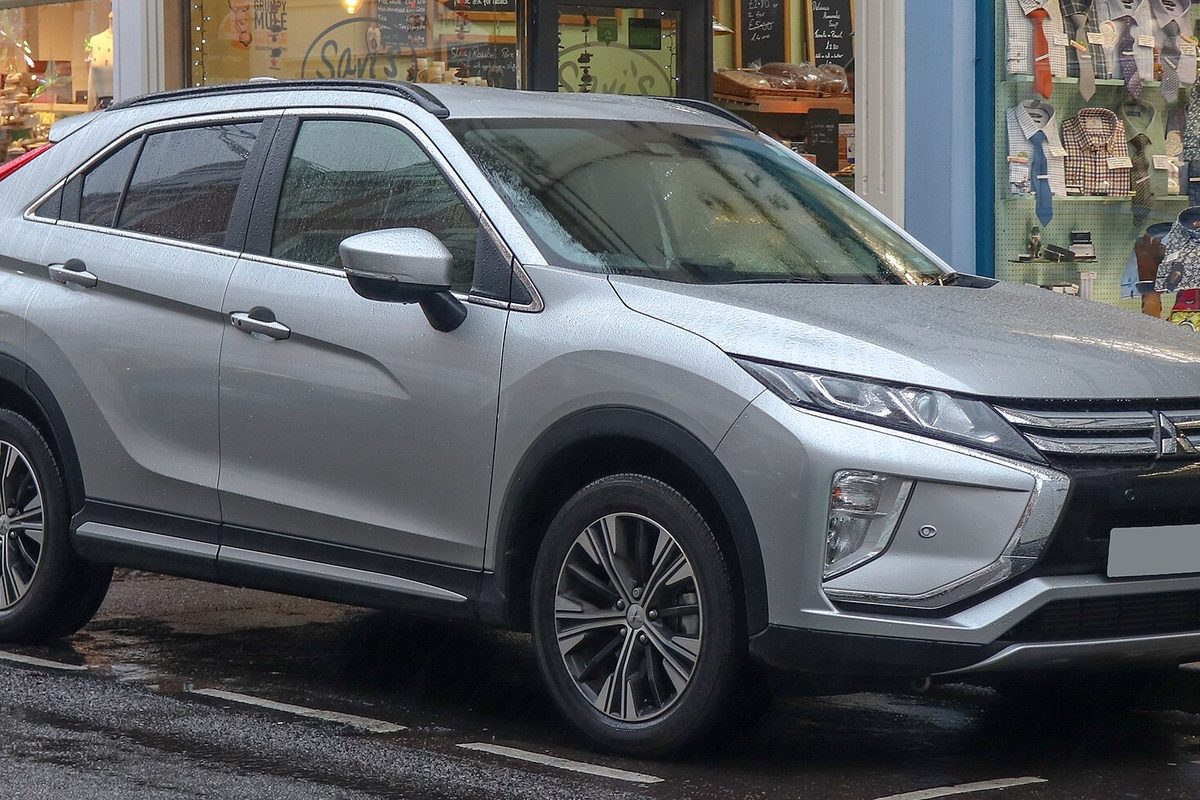 A silver Mitsubishi Eclipse Cross compact SUV parked on a wet street in front of a row of shop windows