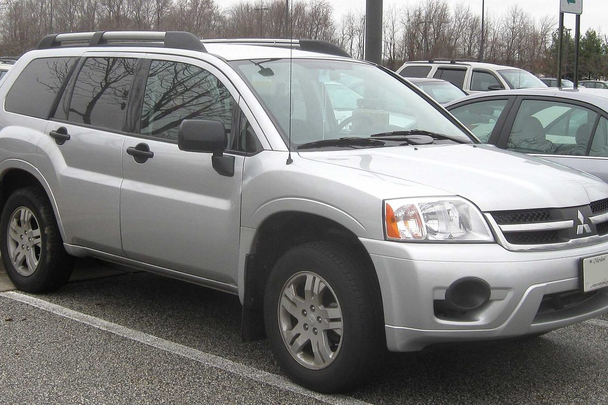 A silver Mitsubishi Endeavor SUV with roof rails, parked in a lot in winter with bare trees behind it