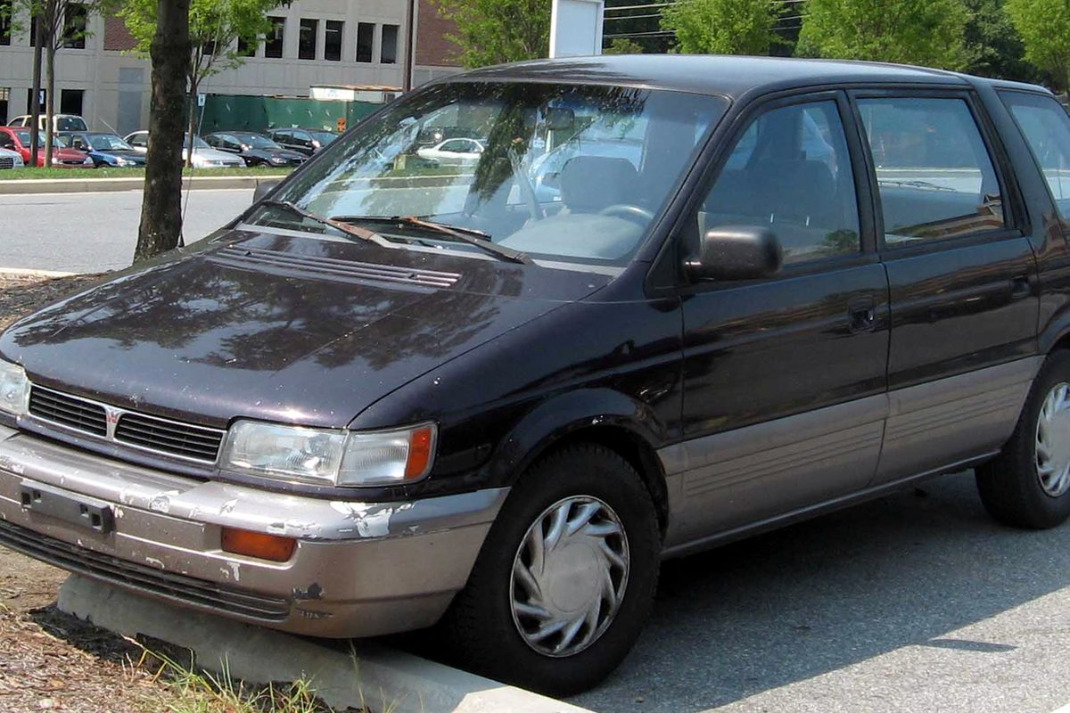 A dark plum Mitsubishi Expo wagon with silver lower trim, wheel covers and a scraped front bumper, parked at a curb