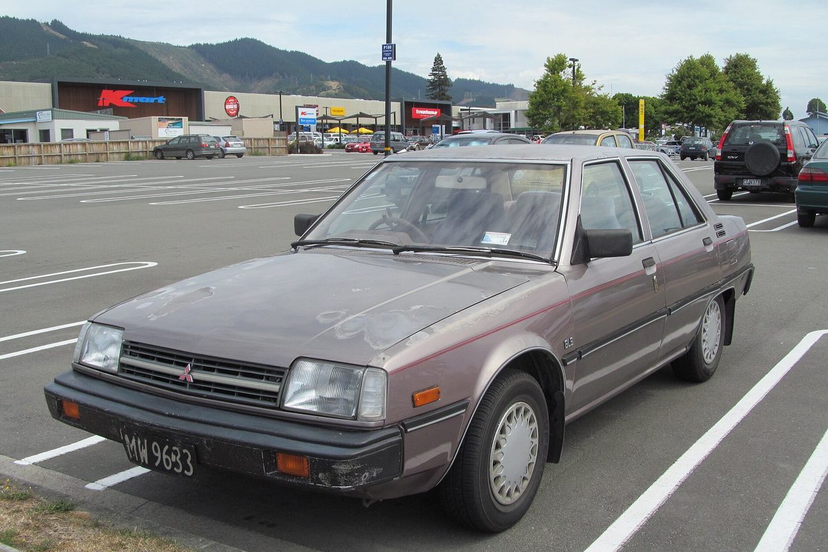A faded taupe Mitsubishi Tredia four-door sedan in a shopping center parking lot
