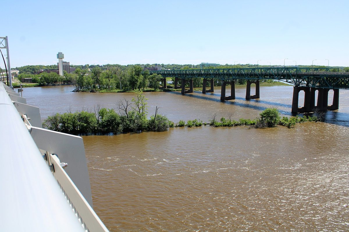 The muddy Mississippi River at Moline, with a line of trees in the water marking the old lock and steamboat canal and a steel truss bridge beyond