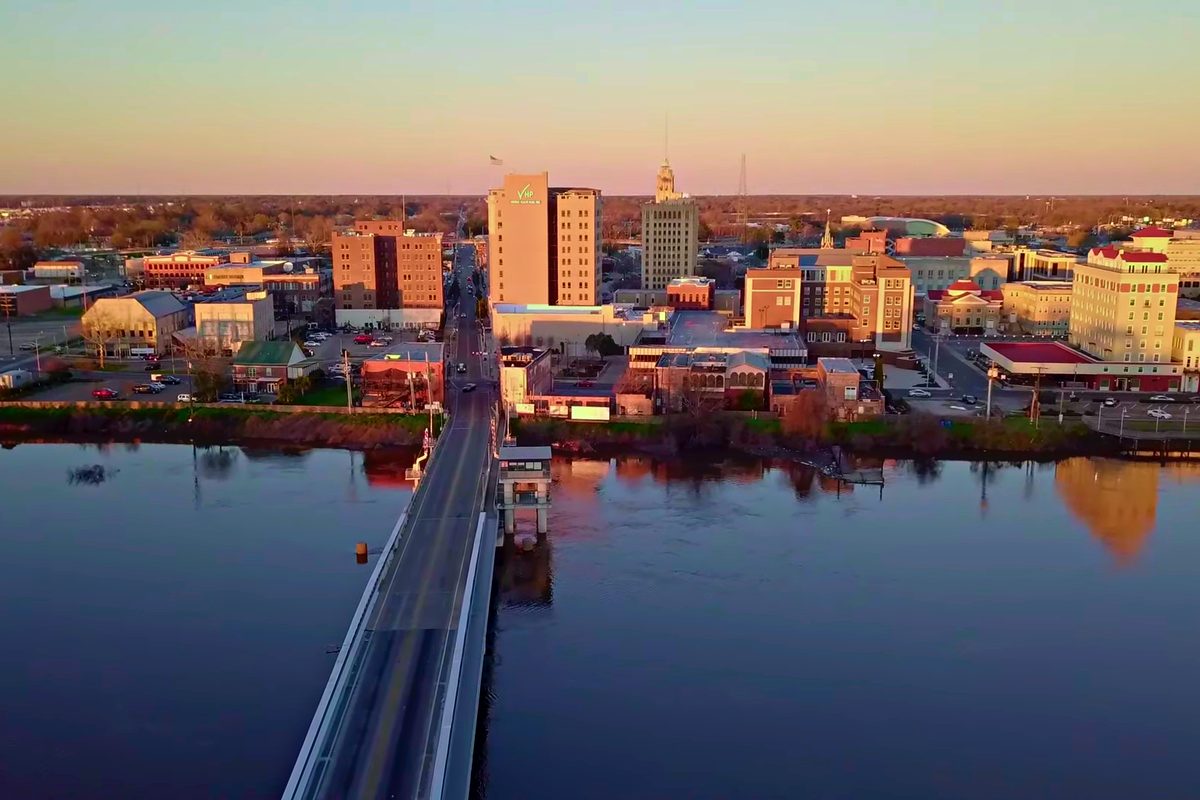 Downtown Monroe's skyline glowing at sunset, seen across the river with a long bridge running into the city