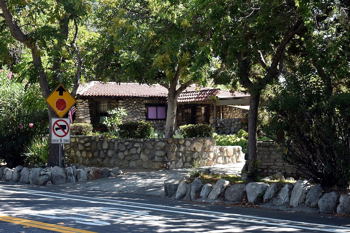 A stone cottage behind a fieldstone wall and boulders, with a weight-limit sign at the curb, in Claremont's Russian Village next to Montclair