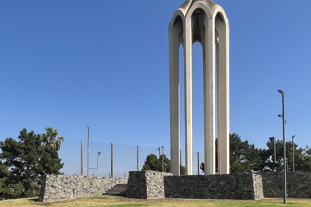 The tall white arched tower of the Montebello Genocide Memorial rising from a stone base under a clear blue sky