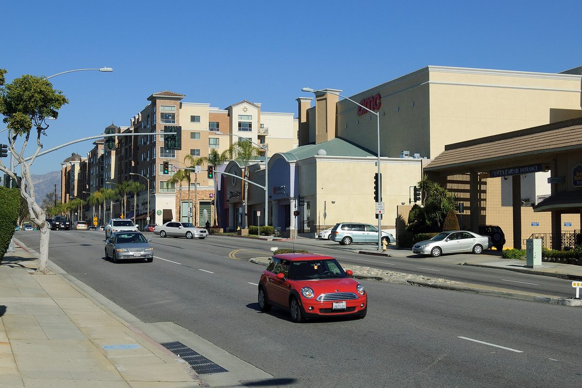 Atlantic Boulevard in Monterey Park on a clear day, with a red compact car in the near lane, palm trees and mid-rise buildings along the street