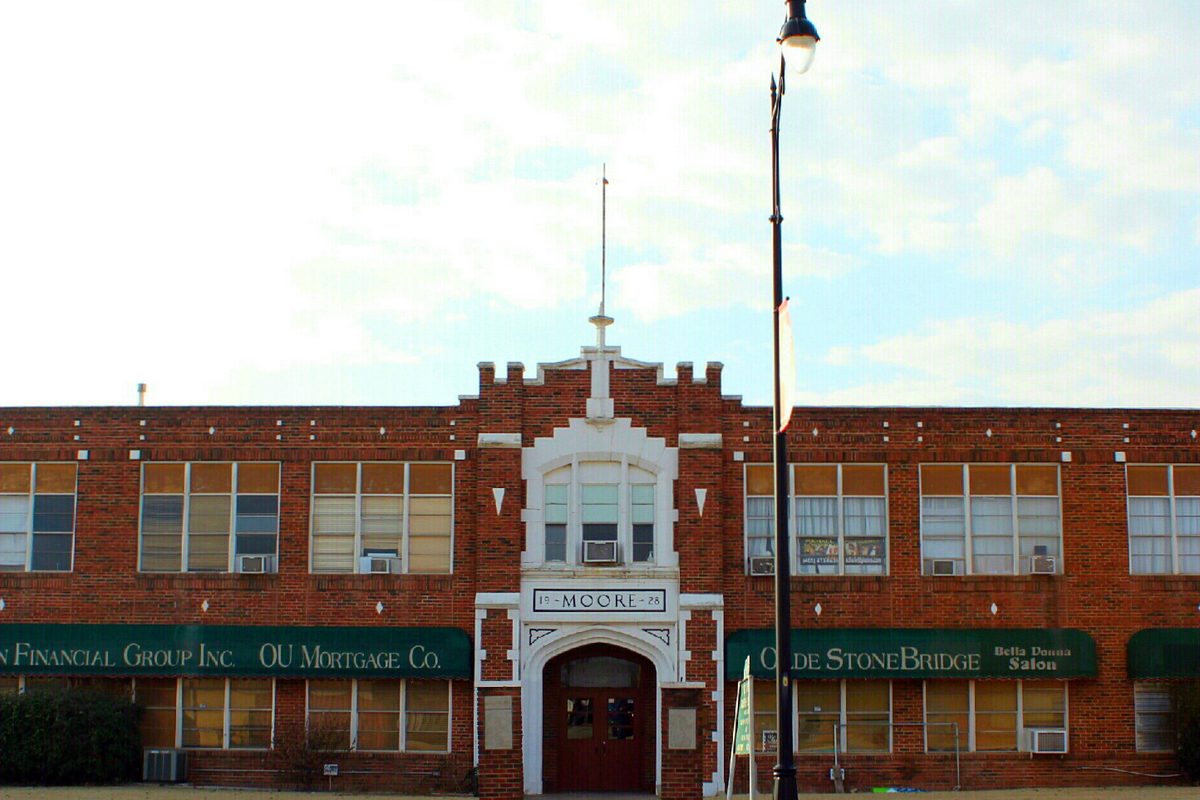 The red brick Moore Public School Building with its white-trimmed arched entrance marked MOORE, under a pale sky
