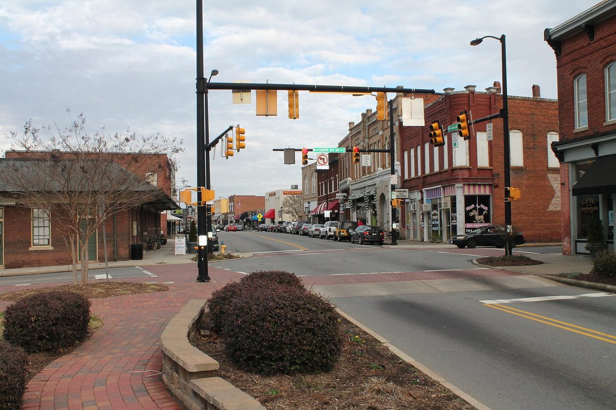Main Street in Mooresville with two-story brick storefronts, traffic lights over the crossing and parked cars under a cloudy sky