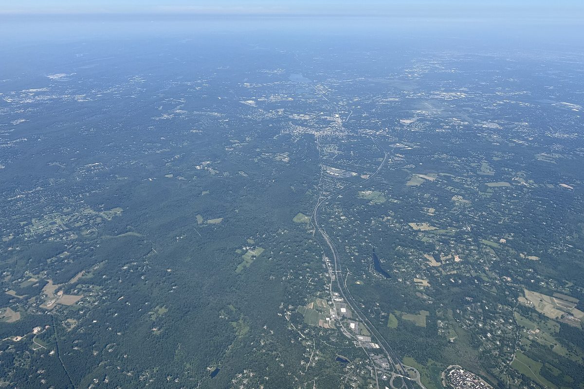 Aerial view over the wooded hills of Harding and Morris townships, with a highway running through and Morristown in the hazy distance