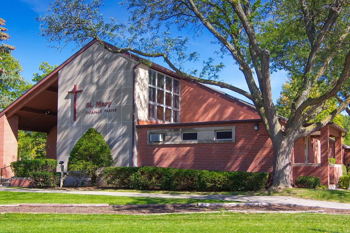 St. Mary University Church in Mount Pleasant, a brick and pale stone building with a red cross on its front and a large tree beside it under a blue sky