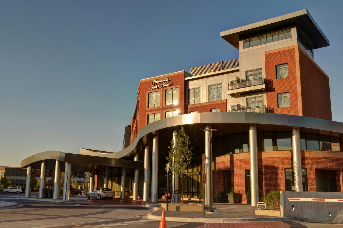 A new brick and white hotel in Mount Prospect with a long curved entrance canopy on silver columns, lit by low evening sun