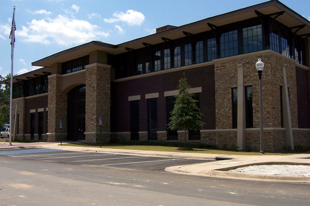 Mountain Brook's Board of Education building, two stories of stone and dark brick with tall windows, a flagpole and a young tree out front under a blue sky