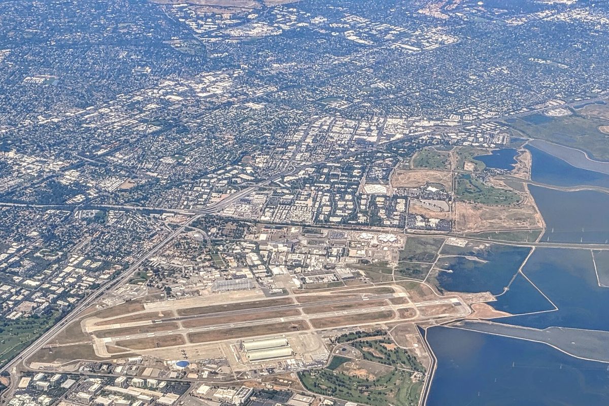 Aerial view of Moffett Field's runways and hangars beside the bay's salt ponds, with Mountain View's office parks and neighborhoods spreading beyond