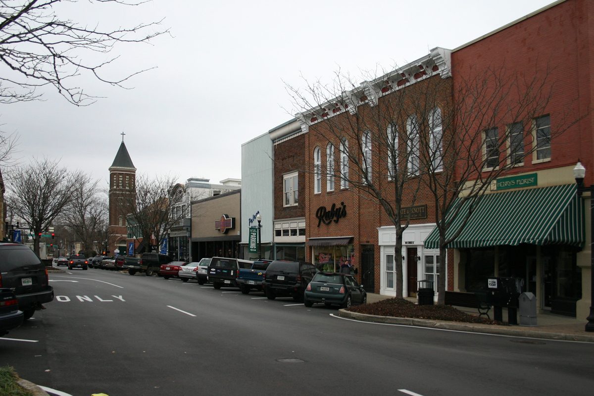 Brick storefronts with a green striped awning along a downtown Murfreesboro street, a church steeple at the far end and bare trees on a gray winter day