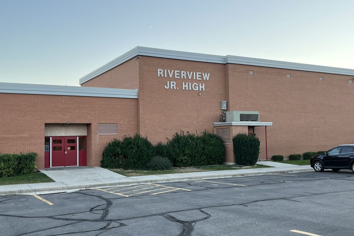 Riverview Junior High School in Murray, a tan brick building with red double doors, seen from the parking lot with a black SUV parked at the right