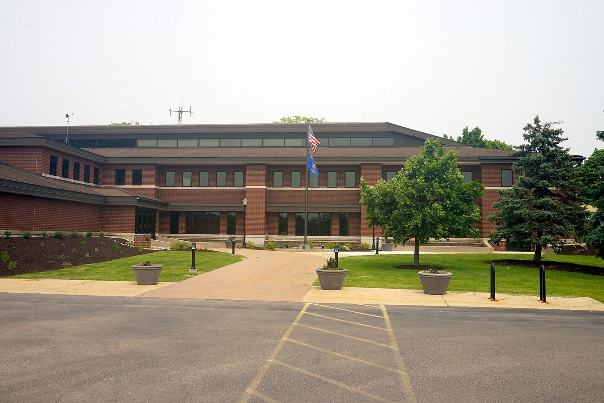 The two-story brick New Berlin City Hall with US and Wisconsin flags out front, seen across an empty parking lot on a hazy day