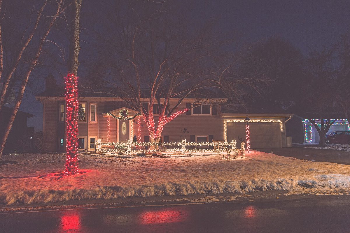 A split-level house on 46th Avenue North in New Hope at night, with red and white holiday lights wrapped around its trees and along the fence, over a snowy yard